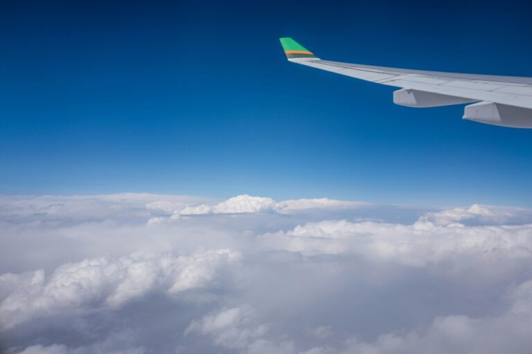 Airplane wing view with vibrant blue sky and scattered clouds, capturing the essence of air travel.